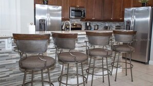 Una cocina moderna con electrodomésticos de acero inoxidable, encimera de mármol y cuatro taburetes de bar con asientos de madera.
