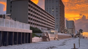 Un hotel frente a la playa con varios edificios altos, una torre de salvavidas y una playa de arena.