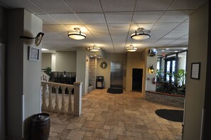 A lobby with a stone-tiled floor, a staircase with a balustrade, and a reception desk.