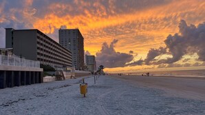 Una playa con un hidrante amarillo, un muelle y edificios al fondo.