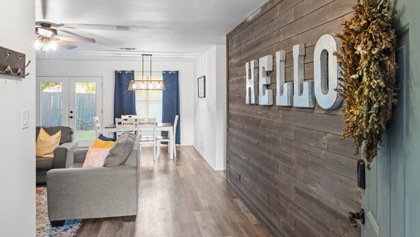 A living room with a gray sofa, a coffee table, and a dining area with a white table and chairs. A large "HELLO" sign is mounted on a wooden wall. - Newly remodeled home w/ a backyard oasis, beautiful hot tub blocks from downtown (Fredericksburg)