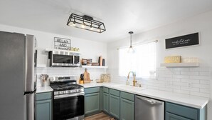 A modern kitchen with a stainless steel refrigerator, a microwave, a stove, and a dishwasher. There are decorative items on the shelves and a rug on the floor. - Newly remodeled home w/ a backyard oasis, beautiful hot tub blocks from downtown (Fredericksburg)