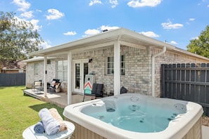 A covered patio area with a hot tub, outdoor seating, and a brick exterior. - Newly remodeled home w/ a backyard oasis, beautiful hot tub blocks from downtown (Fredericksburg)