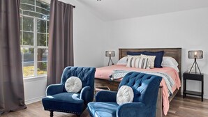 A bedroom with a bed, two armchairs, a nightstand, and a window with curtains. - Newly remodeled home w/ a backyard oasis, beautiful hot tub blocks from downtown (Fredericksburg)