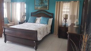 A bedroom with a wooden bed, a painting of a beach scene, and a ceiling fan. - Fun for the entire family.  Explore the island from a down home point of view. (Montego Bay)