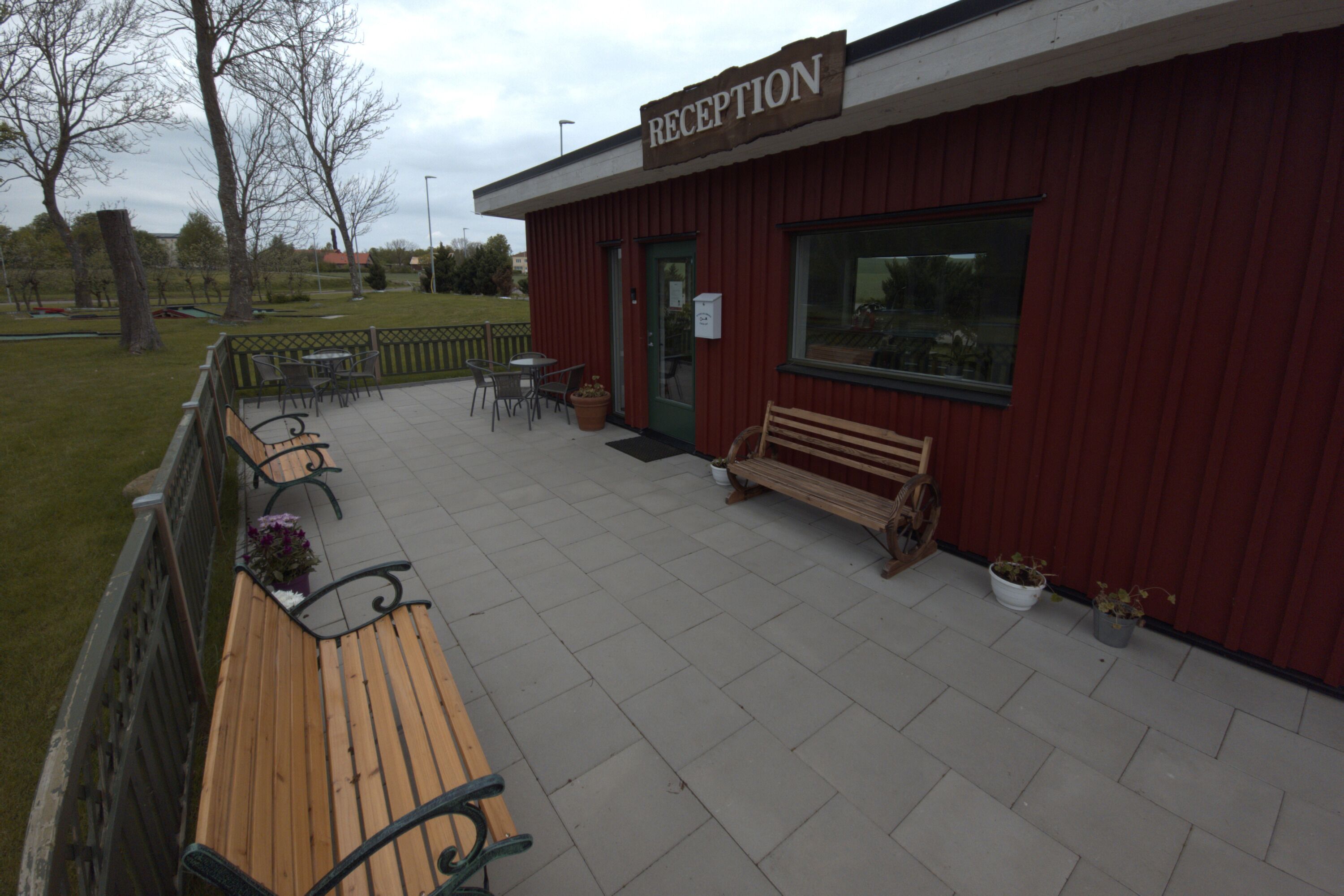 Un espace d’accueil à l’extérieur, avec une façade rouge, un banc en bois et des sièges pour l’extérieur.