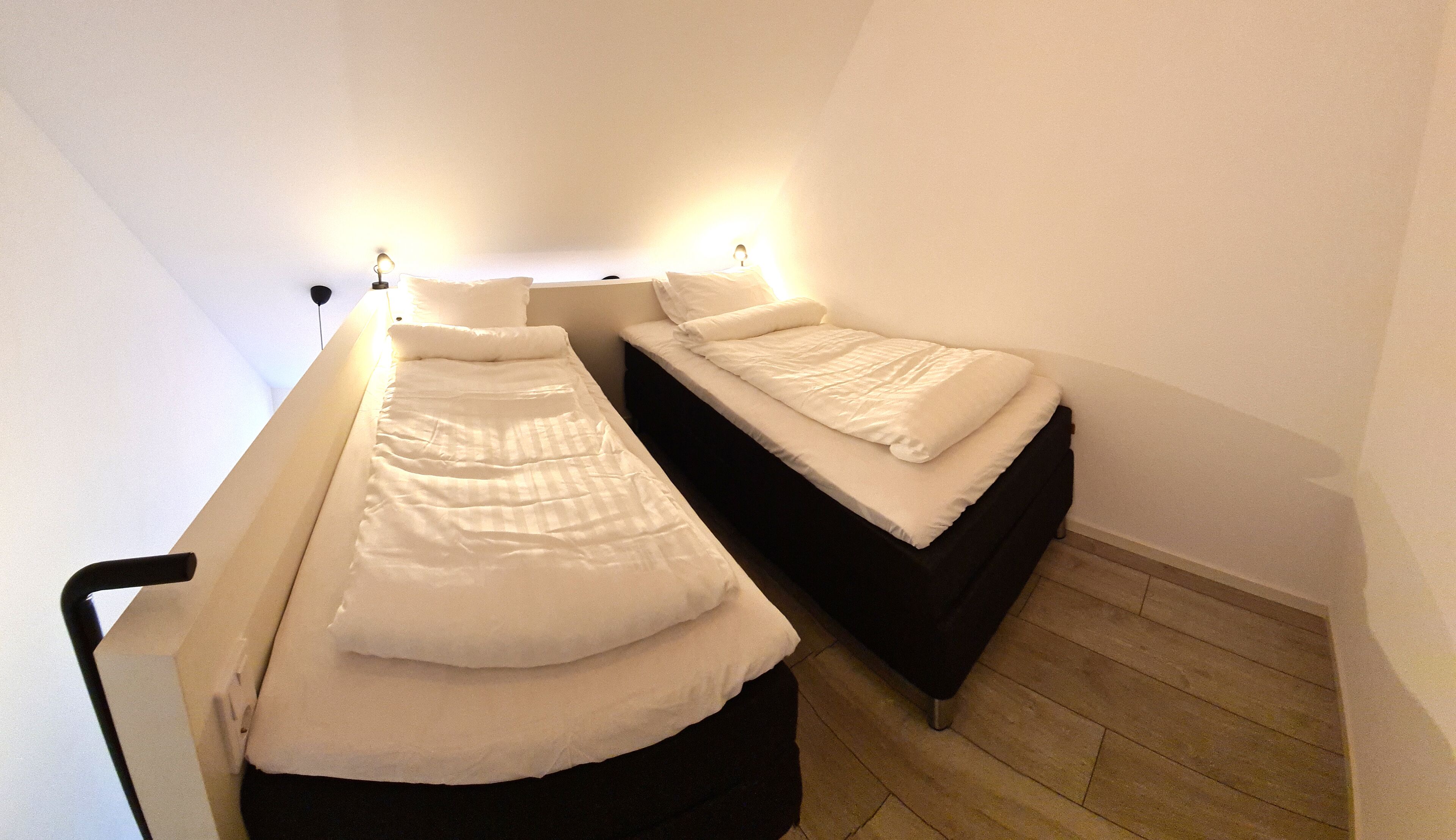 A small, narrow room with two single beds, each with a headboard and pillows.