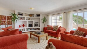 Een woonkamer met rode banken, een salontafel en een boekenkast vol boeken en decoratieve objecten.