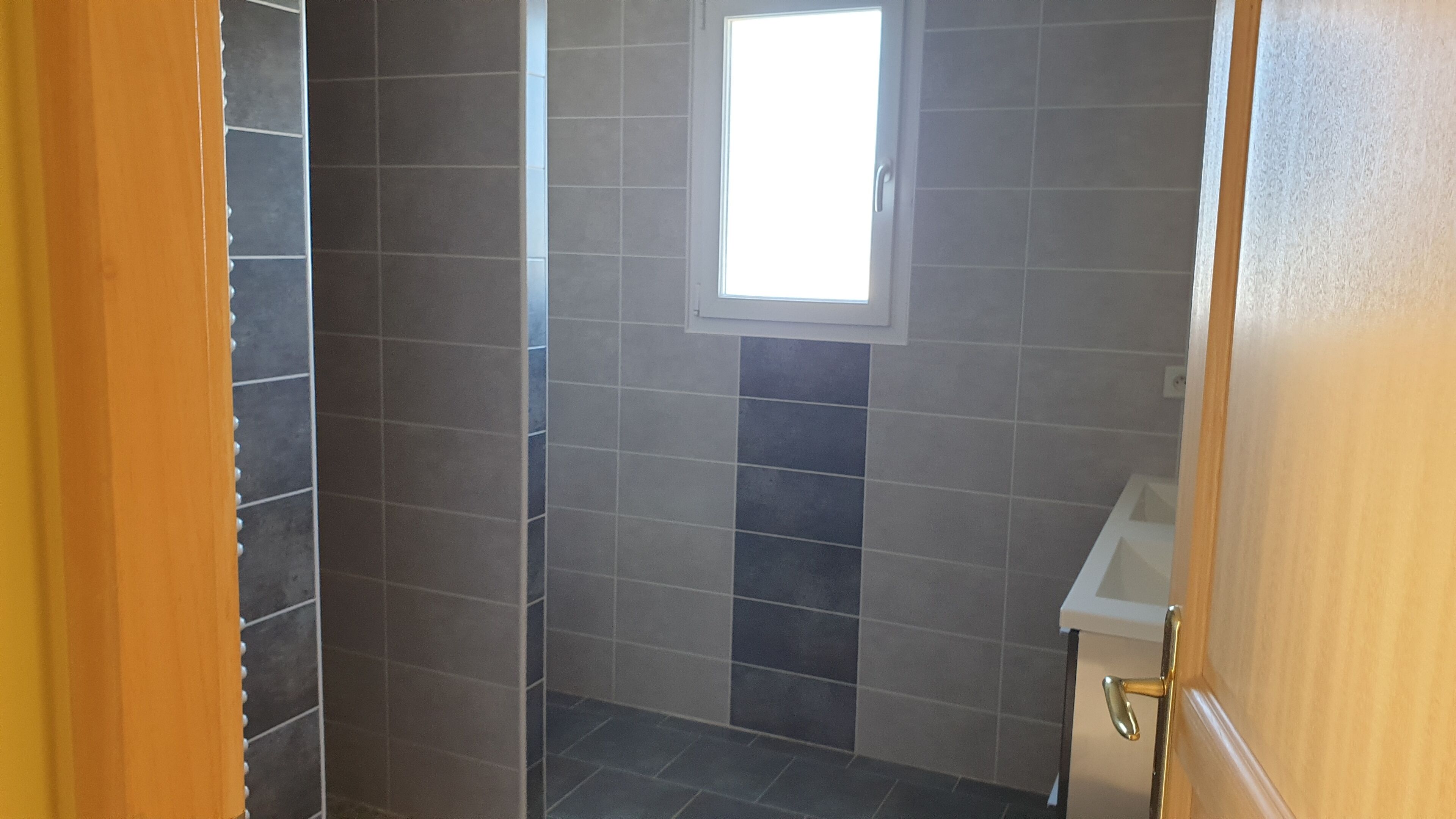 A bathroom with dark tiles, a window, and a sink.
