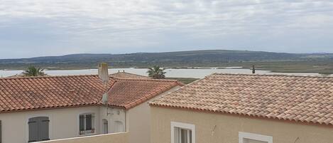 Un quartier résidentiel caractérisé par des toits recouverts de tuiles en terre cuite, un plan d’eau et des collines qui se dessinent à l’horizon.