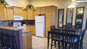 A kitchen with wooden cabinets, a white refrigerator, a sink, and a dining area with a table and chairs. - I Deal Lake Powell Home 3BR, Jacuzzi, BBQ & Firepit (Page)