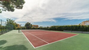 En tennisbane med net, omgivet af grønt og bygninger.
