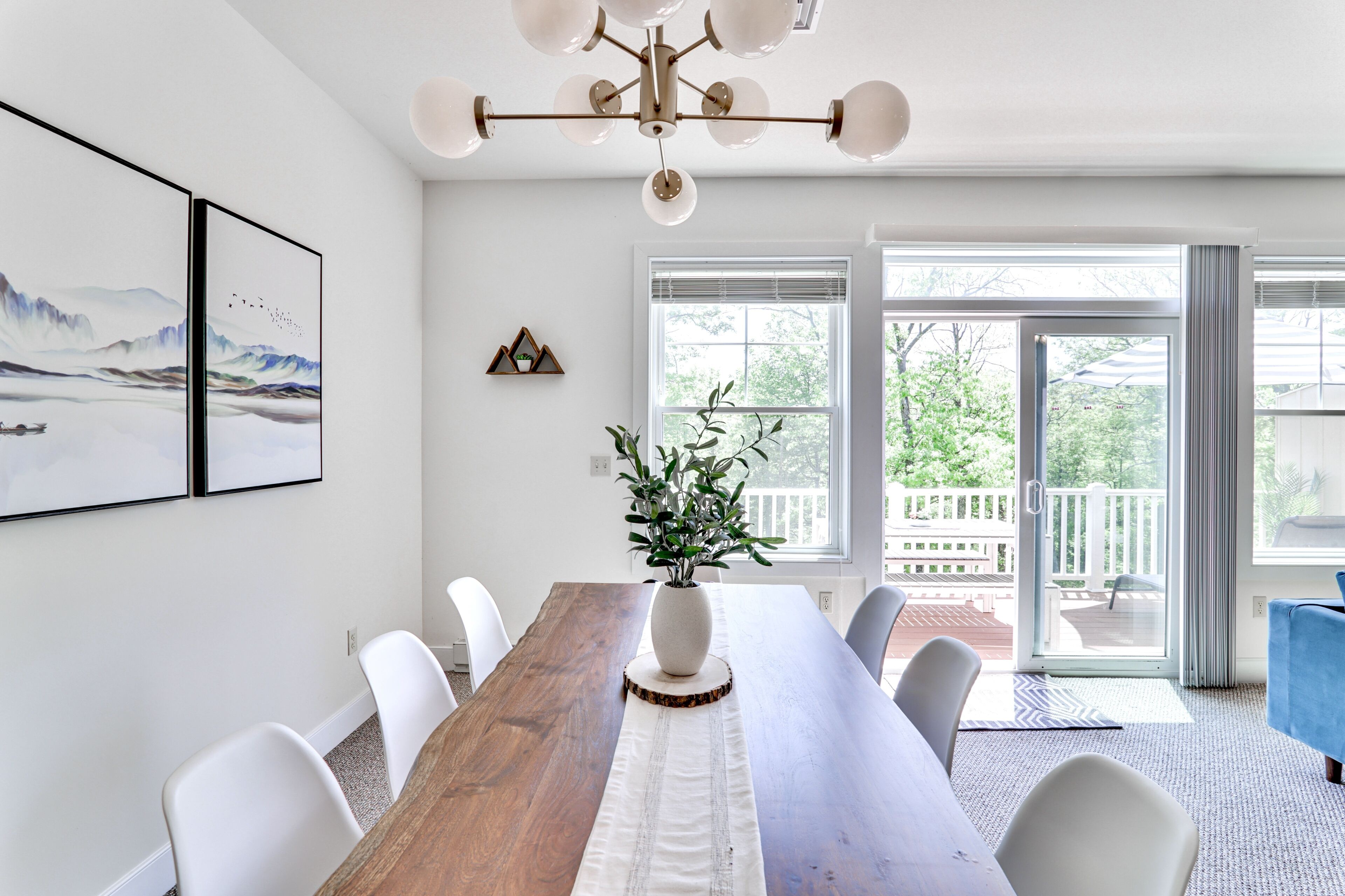A dining area with a wooden table, white chairs, a vase with plants, and a chandelier.