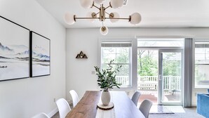 A dining area with a wooden table, white chairs, a vase with plants, and a chandelier. - ⭐️ Spacious Mountaintop Oasis at Camelback | 2,500 SF w/ Game Room, Deck & A/C (Tannersville)