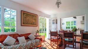 A spacious living room with a red leather sofa, a dining area with wooden chairs, and large windows allowing natural light. - Port Manech house 400 m from the beach, Pouldon cove 100 m away, small river view (Névez)