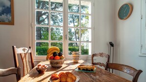 A wooden dining table with a fruit bowl, a plate of pastries, and a stack of plates. - Port Manech house 400 m from the beach, Pouldon cove 100 m away, small river view (Névez)