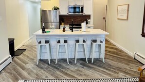 A modern kitchen with a central island, bar stools, a refrigerator, a microwave, and a brick wall backsplash.