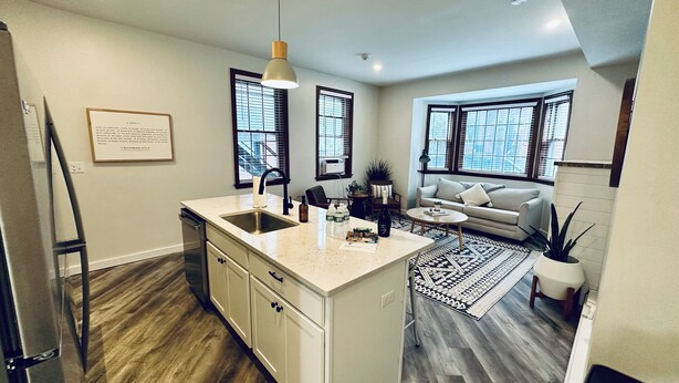 A modern kitchen with a central island, a dining area with a sofa and coffee table, and large windows providing natural light.