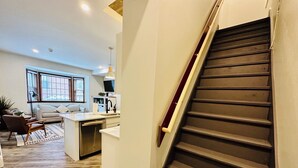 A modern interior with a staircase, a kitchen area, and a living room with a sofa and a coffee table.