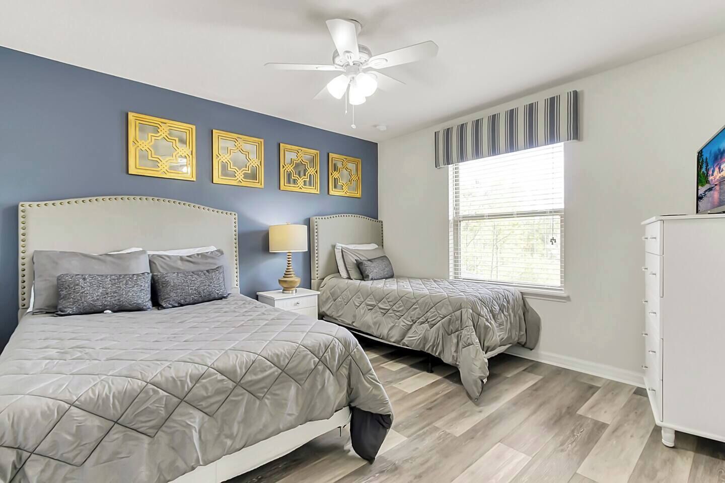 Quarto com duas camas, um ventilador de teto e uma janela com persianas.