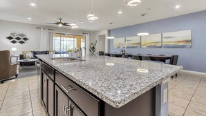 Una cocina moderna con una isla de granito, luces empotradas en el techo y vistas al área de comedor.