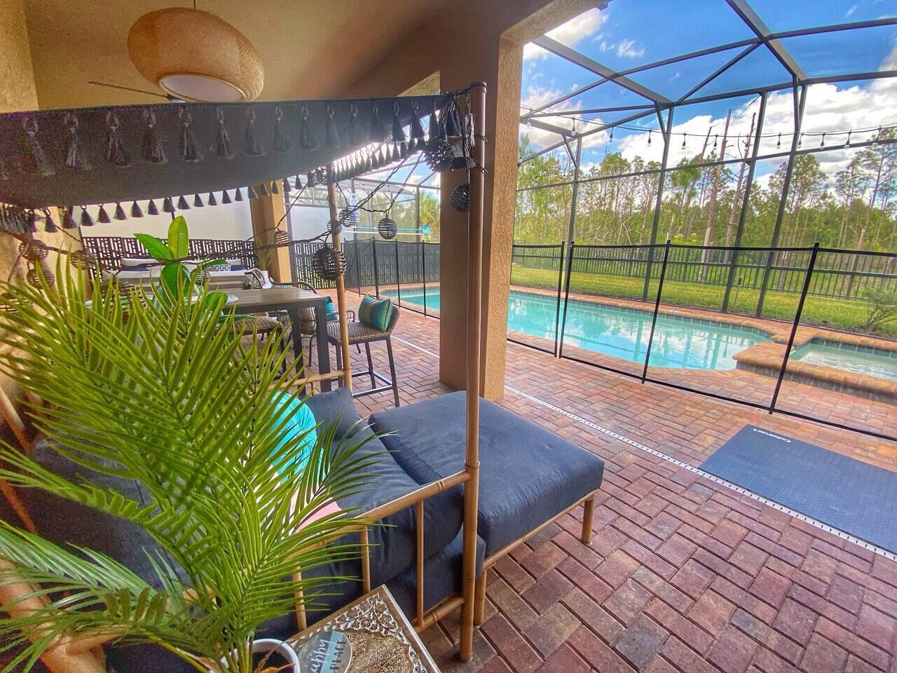 A covered outdoor seating area with a pool view, a table with chairs, and a potted plant.