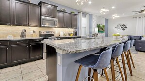 Una cocina moderna con armarios oscuros, encimeras de granito, una campana extractora de acero inoxidable y una isla grande con taburetes de bar.