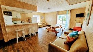 A compact living space with a kitchenette, a wooden dining table, a sofa, and a TV mounted on the wall.