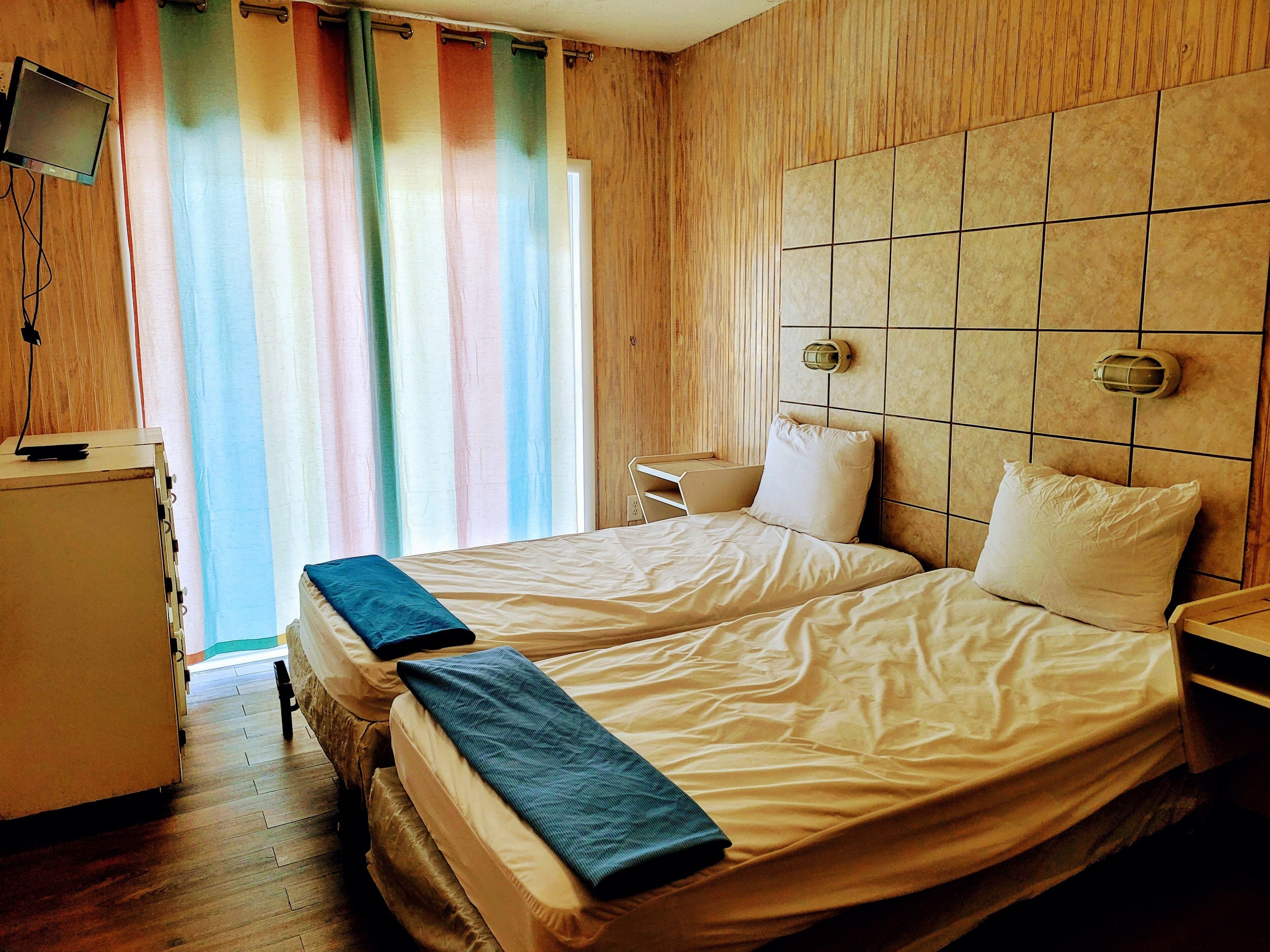Habitación de hotel con una cama doble, un escritorio pequeño con televisión y una ventana con cortinas coloridas.