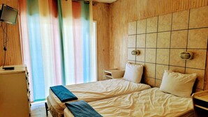 A hotel room with a double bed, a small desk with a TV, and a window with colorful curtains.