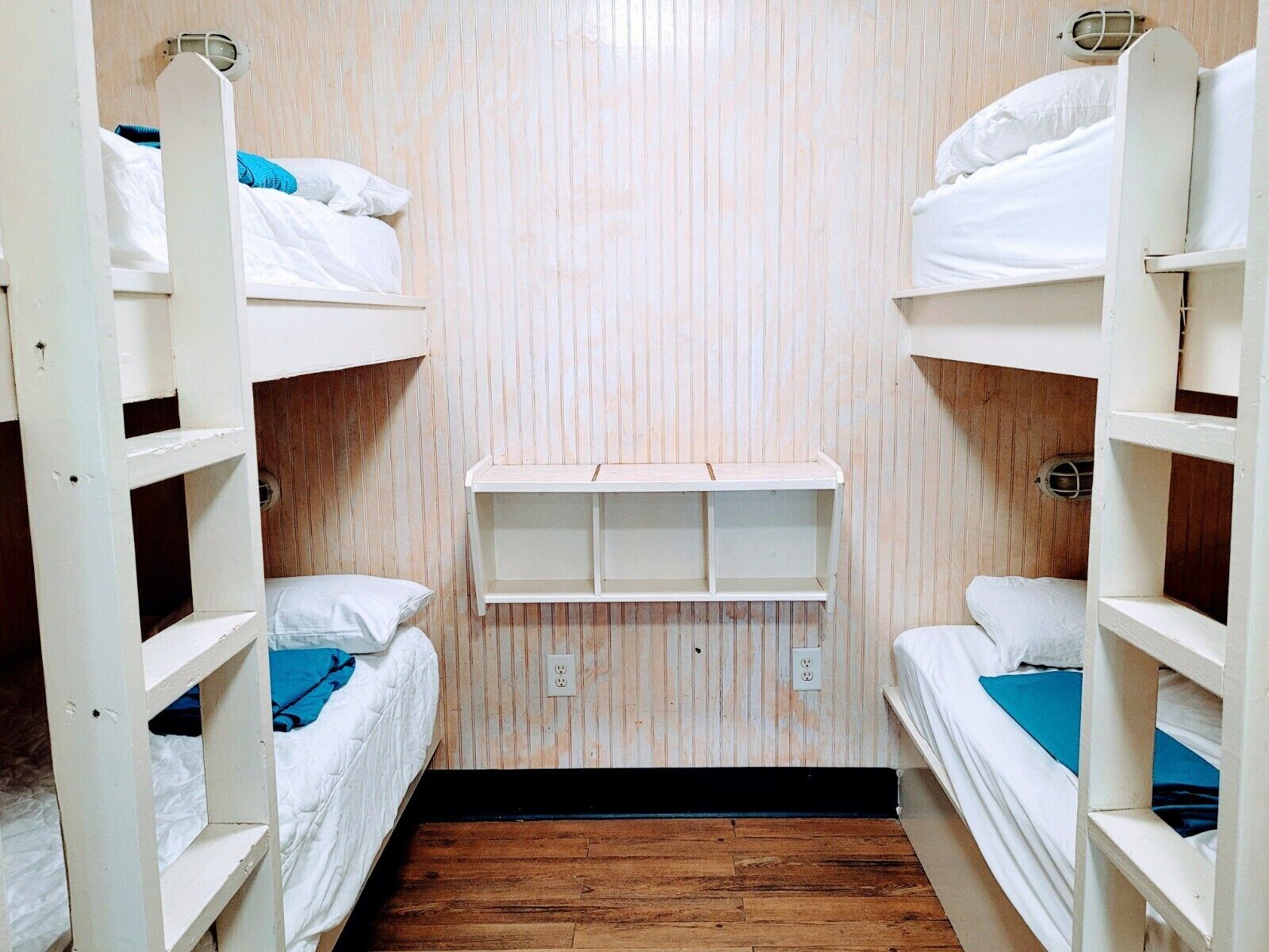 A bunk bed room with wooden walls and a shelf unit in the center.
