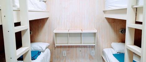 A bunk bed room with wooden walls and a shelf unit in the center.