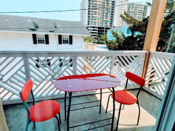 Een balkon met een tafel en twee stoelen, met uitzicht op een woongebied met meerdere gebouwen.