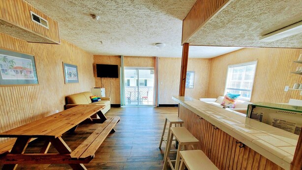 A wooden interior with a long table and benches, a counter with a sink, and framed pictures on the walls.