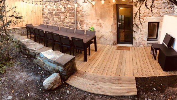 An outdoor patio with a wooden deck, stone walls, and a table with chairs. - Gîte Aux Portes du Sancy, en Auvergne, Jusqu'à 15 Personnes (Montaigut-le-Blanc)