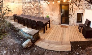 Une terrasse extérieure dotée d’une plateforme en bois, de murs en pierre et d’une table avec des chaises.