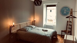 A bedroom with a bed, bedside lamps, a window, and a wall sign. - Gîte Aux Portes du Sancy, en Auvergne, Jusqu'à 15 Personnes (Montaigut-le-Blanc)