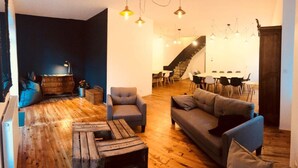 A modern living room with a wooden floor, a sofa, armchairs, and a coffee table. There is a staircase leading to a dining area with a table and chairs. - Gîte Aux Portes du Sancy, en Auvergne, Jusqu'à 15 Personnes (Montaigut-le-Blanc)