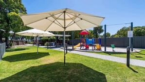 A playground with a slide and climbing structures, surrounded by a grassy area with umbrellas. - FiftyTwo @ Cape View is the perfect family or couples getaway accommodation (BROADWATER)