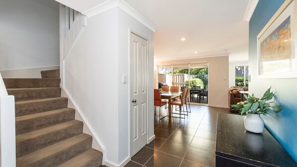 A modern home interior with a staircase, a dining area, and a kitchen visible through glass doors.
