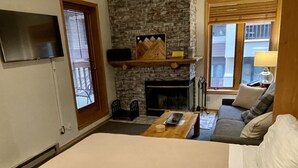 A cozy living room with a fireplace, a flat-screen TV mounted on the wall, a sofa, and a coffee table. - SKI-IN/OUT Charming studio condo steps to lift in the heart of Purgatory Resort! (Durango)