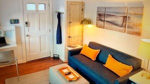 Un salon avec un canapé bleu, des coussins orange, un meuble en bois et un tableau accroché au mur.