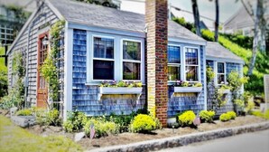 Une petite maison de plain-pied, avec une cheminée en briques, des fenêtres de toit et un petit porche agrémenté de jardinières.