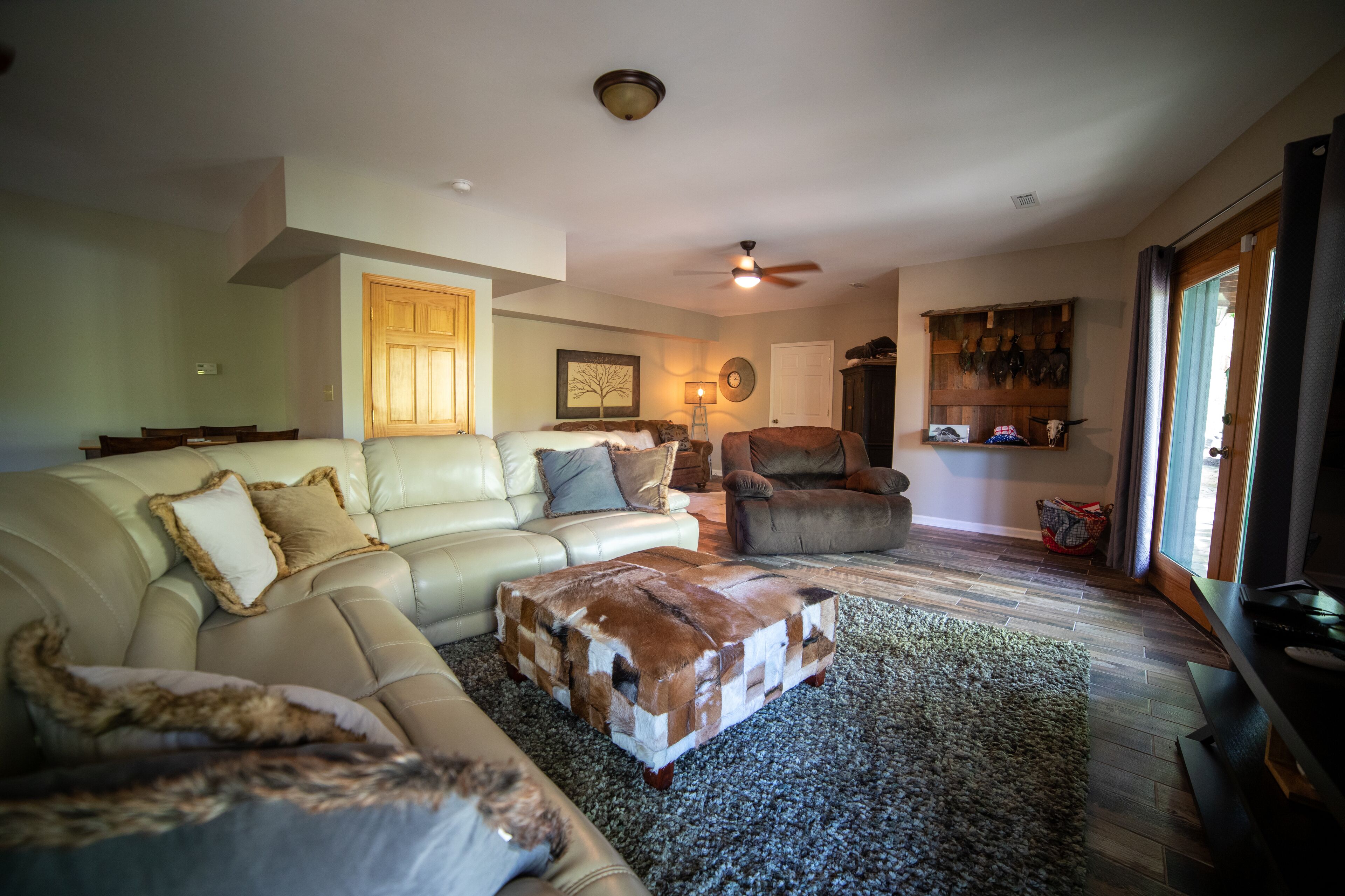 A living room with a beige leather sofa, a brown leather ottoman, a wooden coffee table, and a television on a wooden stand.