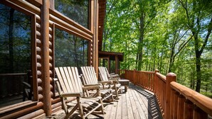 Eine Holzterrasse mit Schaukelstühlen und großen Fenstern mit Blick auf einen Wald.
