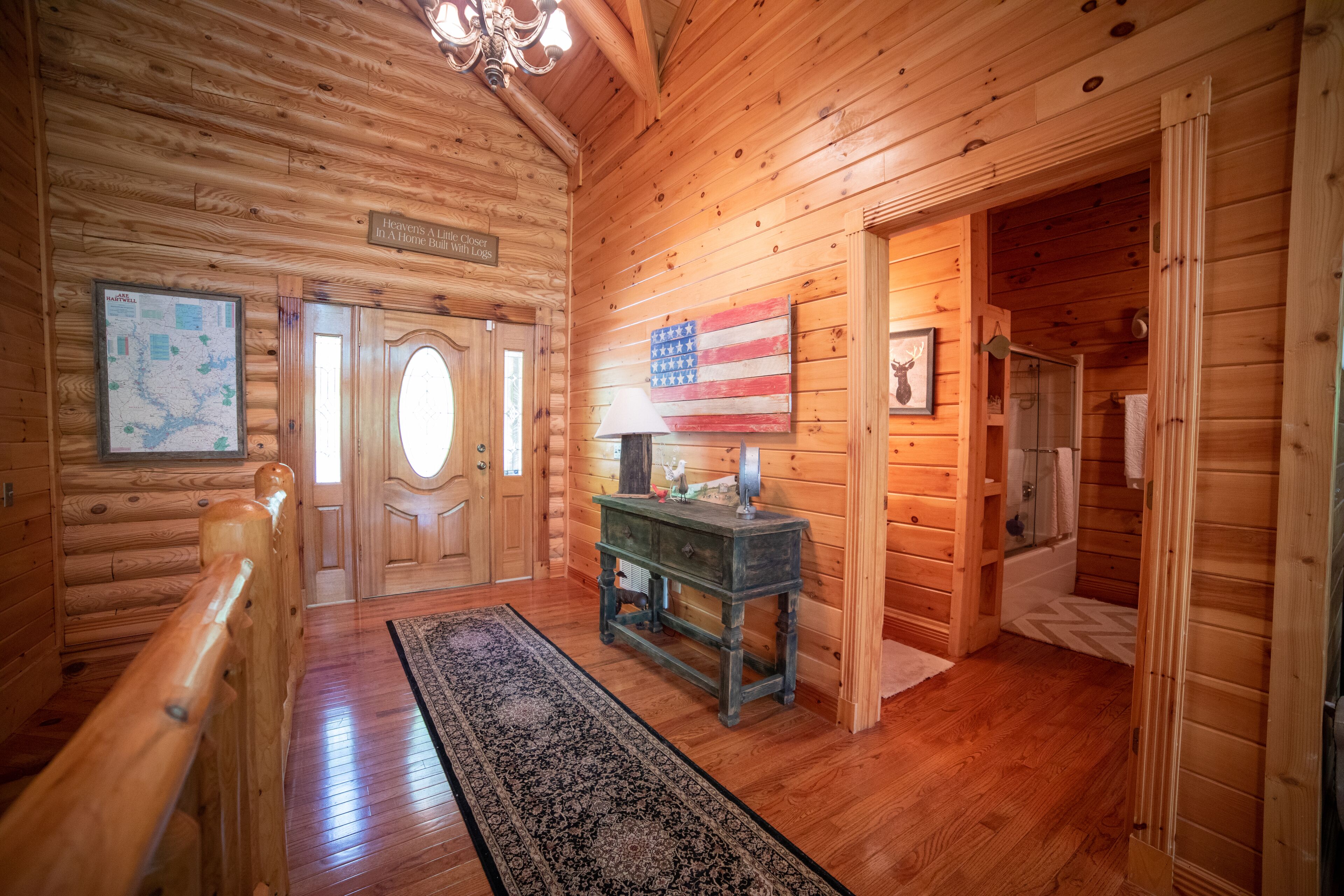 L’intérieur d’un chalet en bois, avec un escalier en bois, une carte accrochée au mur, un drapeau américain et une petite table sur laquelle se trouve une lampe.