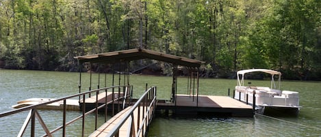 Une jetée en bois s’avançant dans un lac, avec un espace de repos abrité et un bateau amarré à proximité.