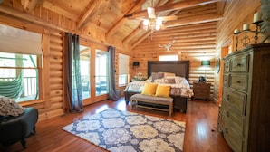Ein Schlafzimmer in einer Blockhütte mit einem großen Bett, einer Bank, einem Schminktisch und einem Deckenventilator.