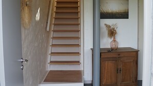 A staircase with wooden steps leading to a landing, a wooden cabinet with a vase, and a wall-mounted artwork. - Charming house in the countryside (Havelange)