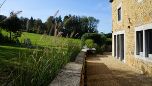 A stone building with a gravel path leading to a wooden table and chairs. - Charming house in the countryside (Havelange)